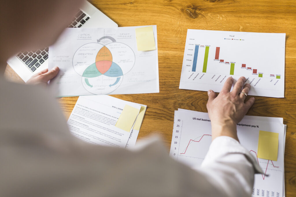 businessperson-s-hand-analyzing-graph-wooden-desk