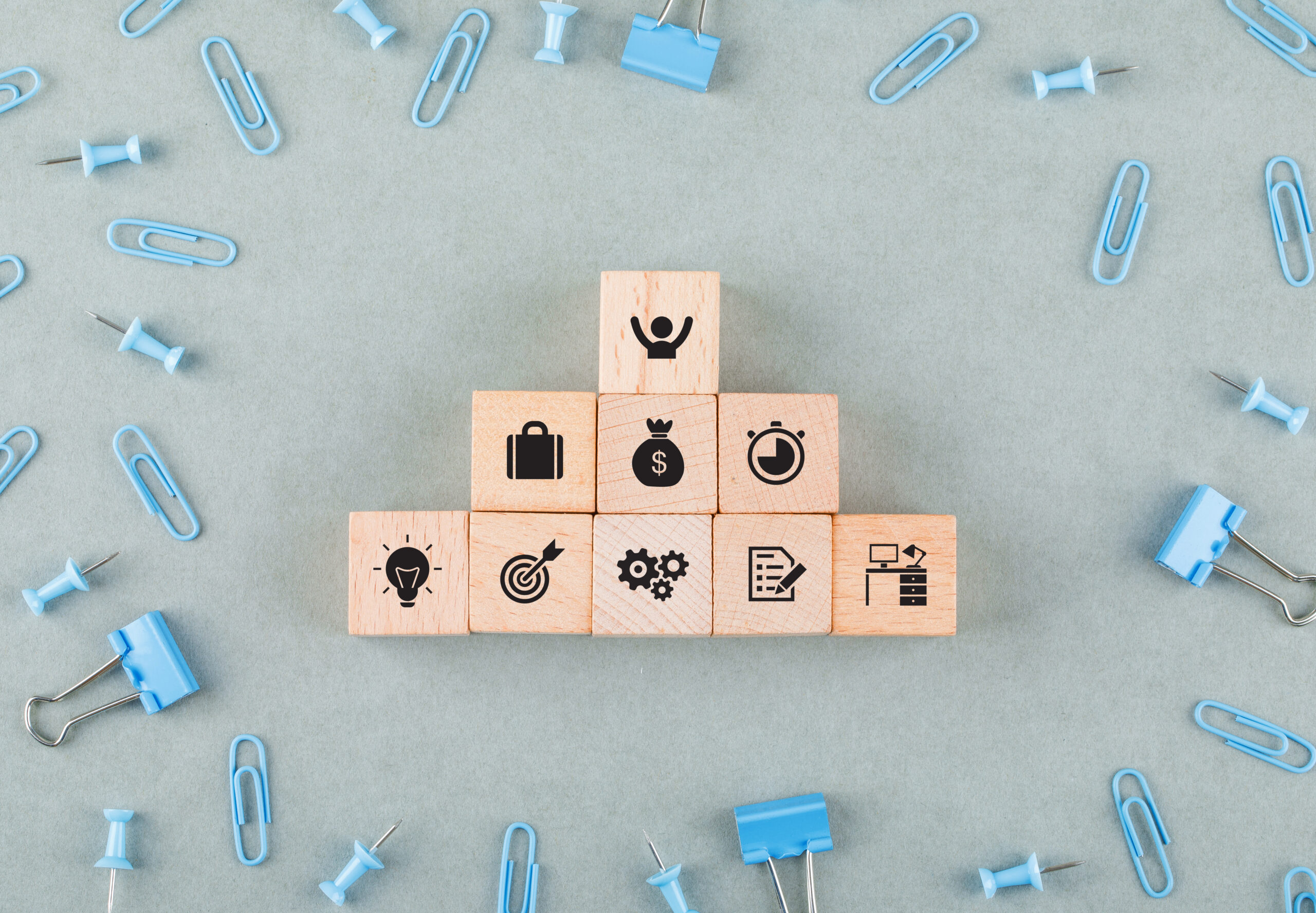 Conceptual of business office with wooden blocks with icons, paperclips, binder clips on sage color background top view. horizontal image